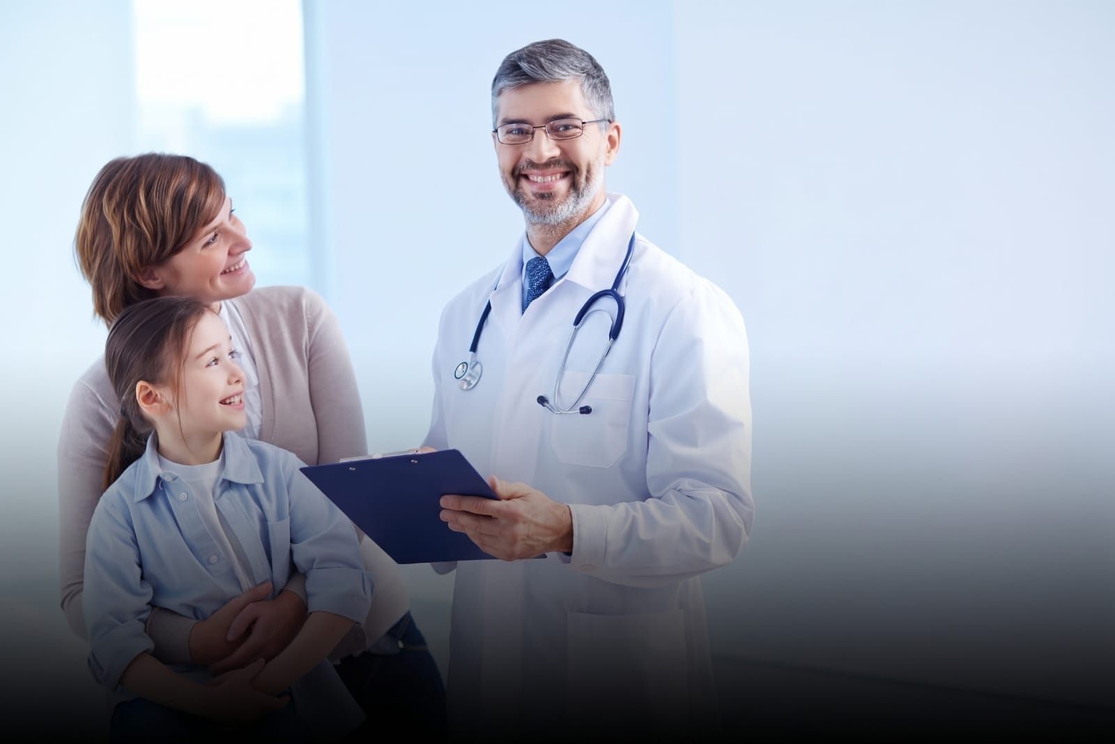 Médico sonriente atendiendo a una madre y su hija en consulta